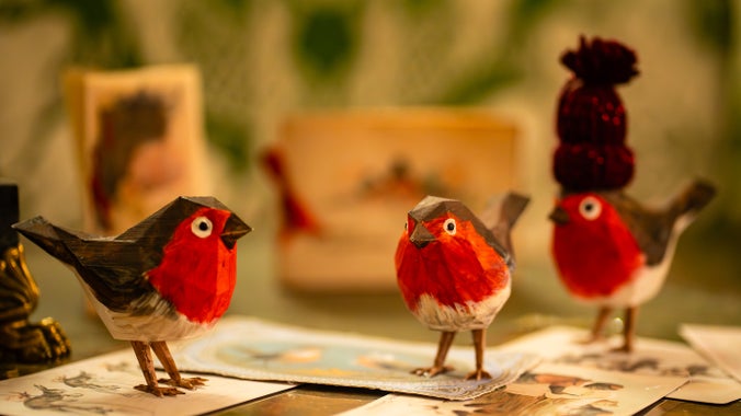 An image of three paper mache robins sitting on a table. One is wearing a woolly hat.